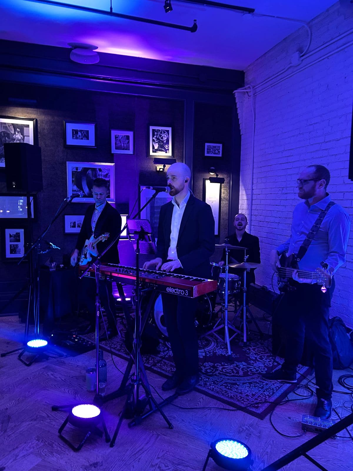 Supersonic Hearts playing under blue light in front of the gallery wall: keys, guitars and drums.