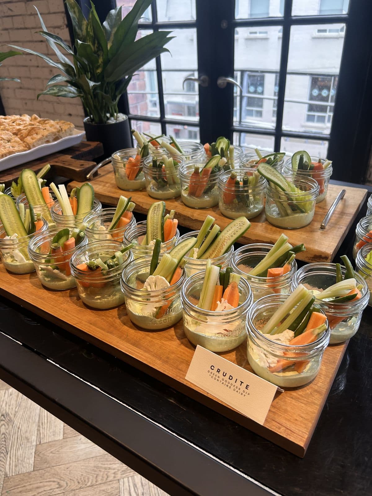 Glass jars of cucumber, carrot and celery sticks standing in green goddess sauce, lined up on wooden boards.