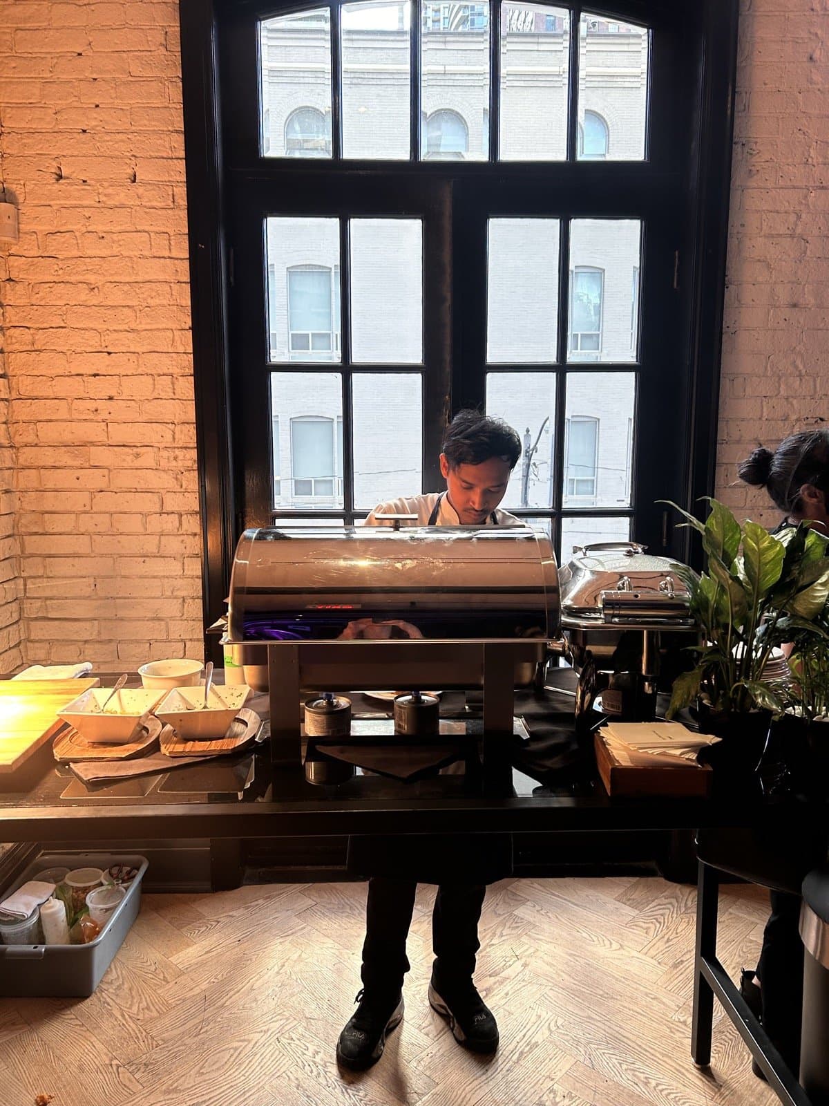 A Storys chef at the hot station, steel chafing dishes set on a long counter in front of a tall arched window.