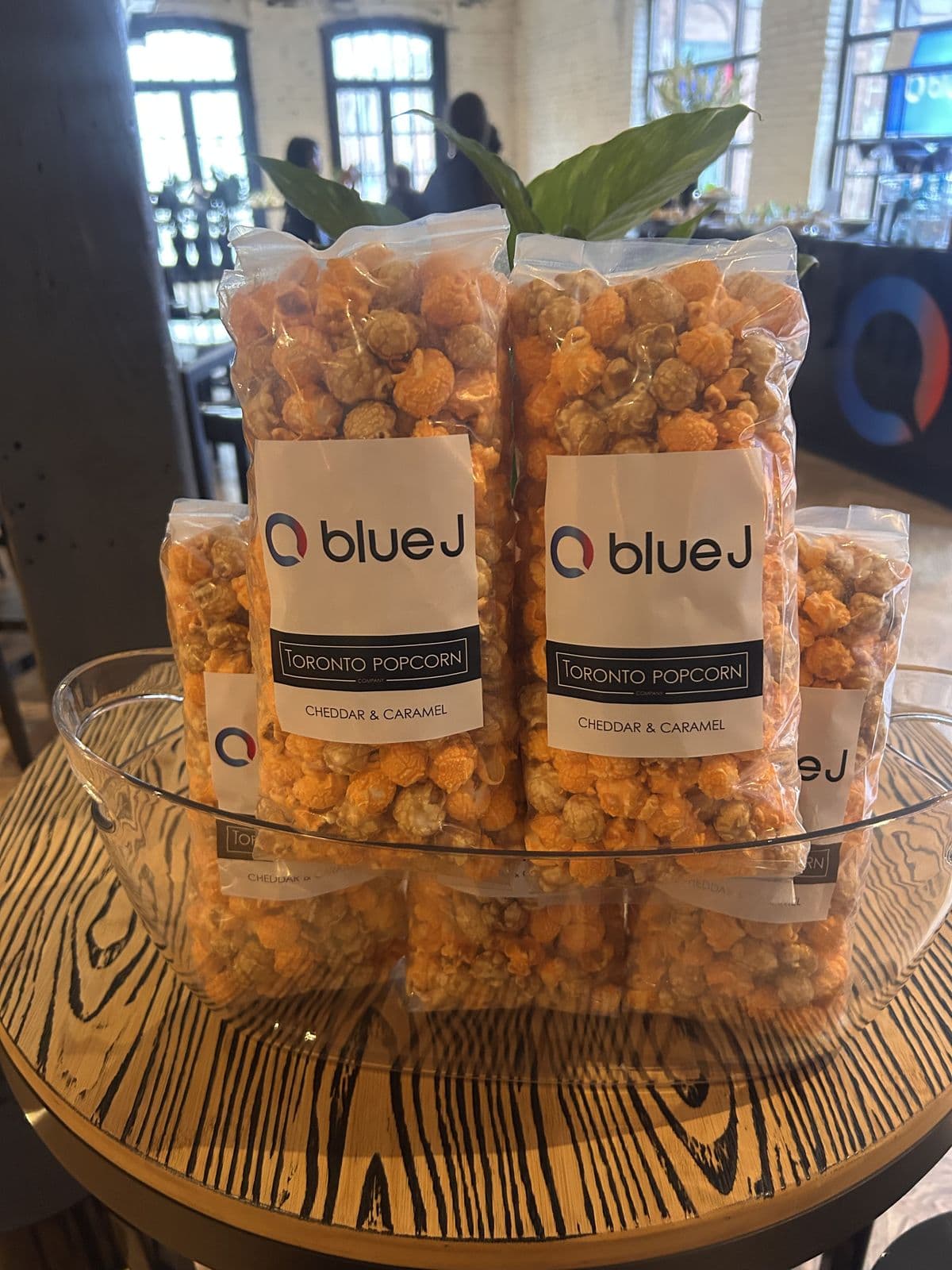 Clear bags of cheddar and caramel popcorn labelled Blue J and Toronto Popcorn, stacked in a glass bowl.