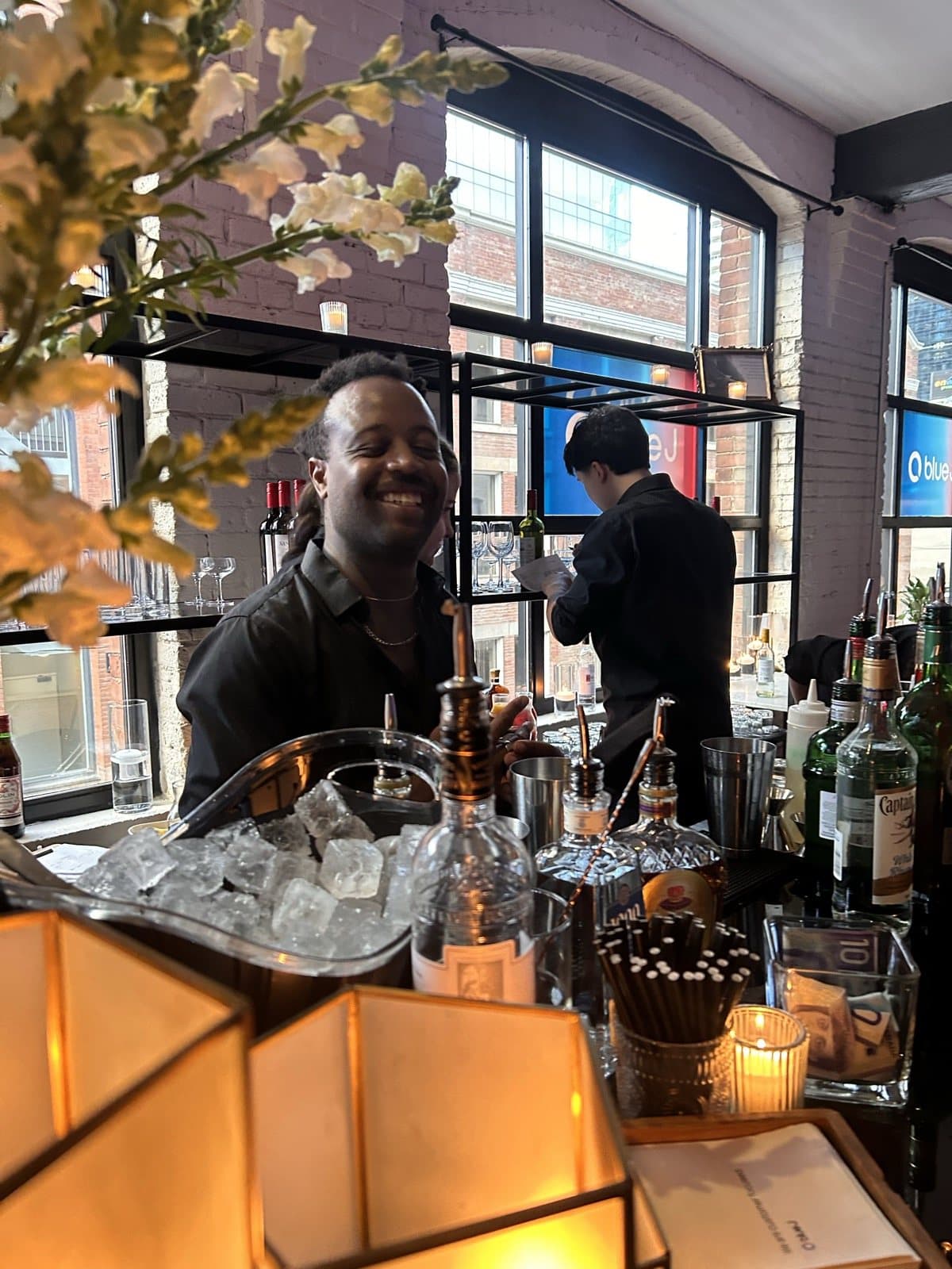 A Storys bartender smiling behind the reception bar, an ice well and bottles in front of him and a Blue J graphic in the arched window behind.