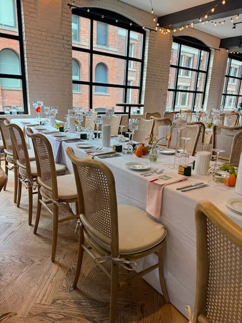 The dinner room photographed from the far end, showing the full run of the table and the brick wall beyond.