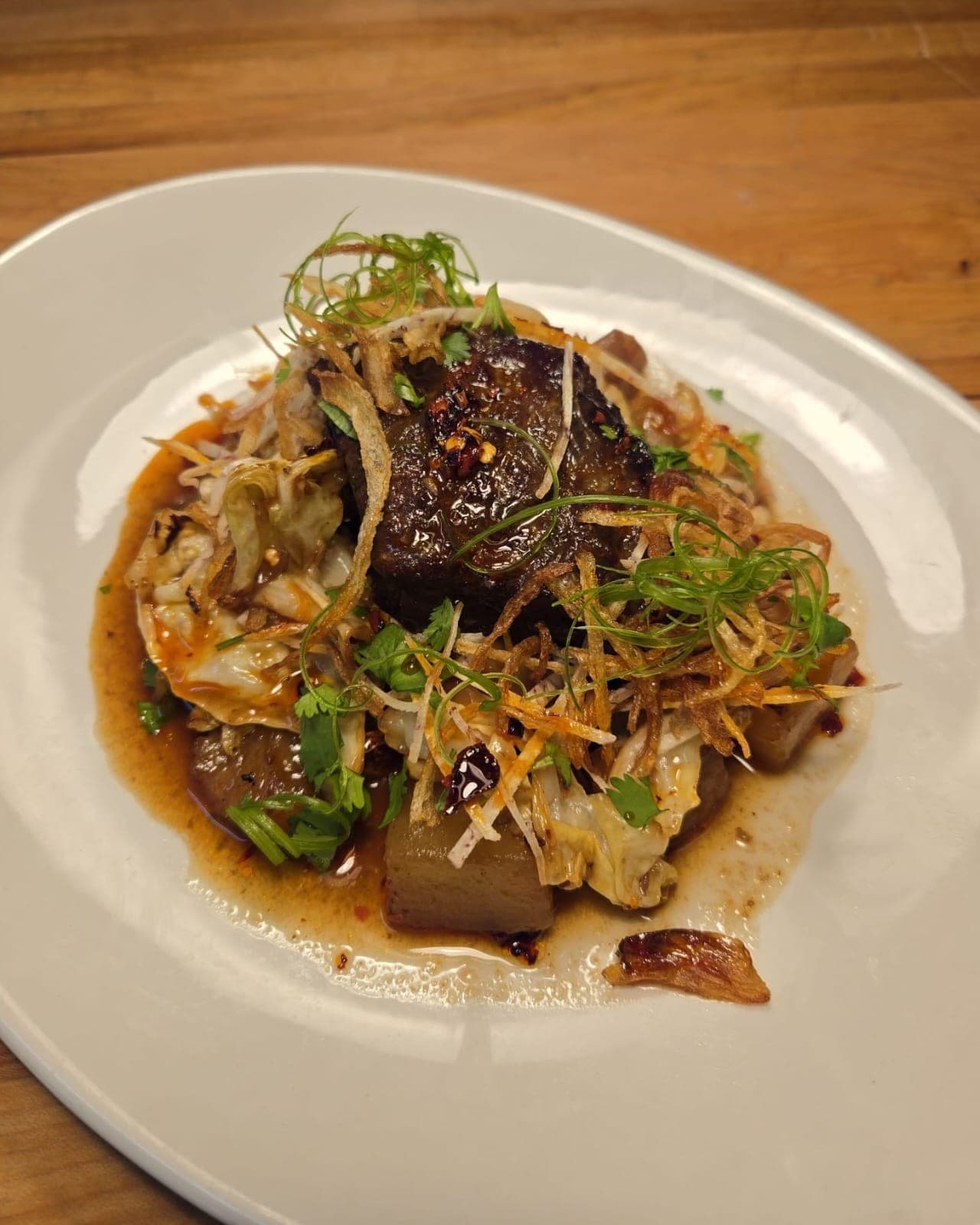 Braised short rib plated with daikon and cabbage in a dark, glossy sauce.