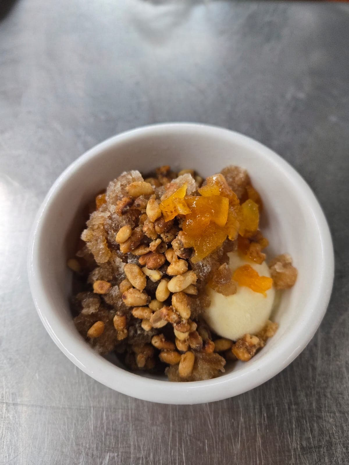A scoop of pale sujeonggwa tea ice cream topped with candied pine nuts and persimmon.
