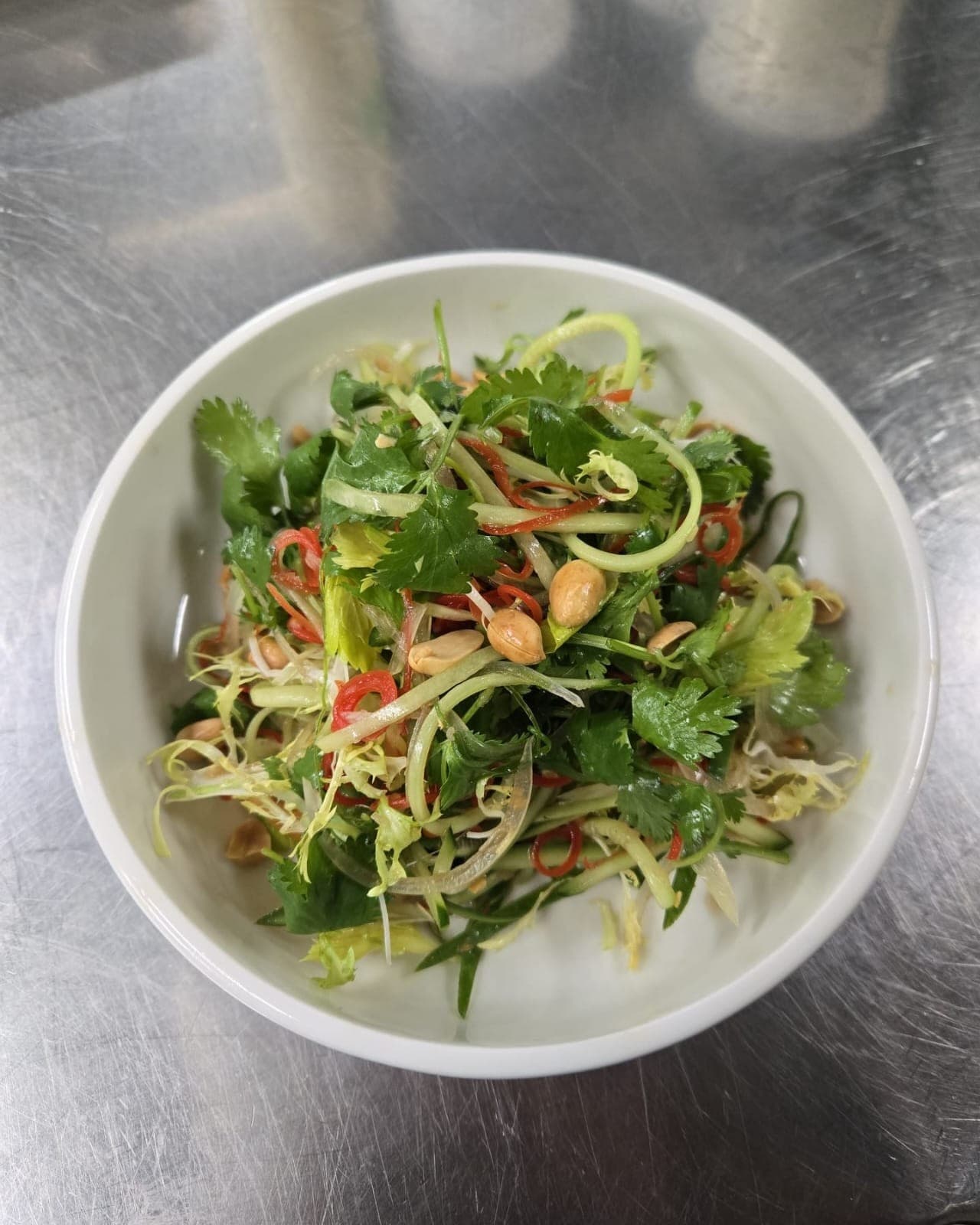 Tiger salad in a shallow white bowl: shredded cucumber and celery with coriander leaves, rings of red chilli and roasted peanuts.