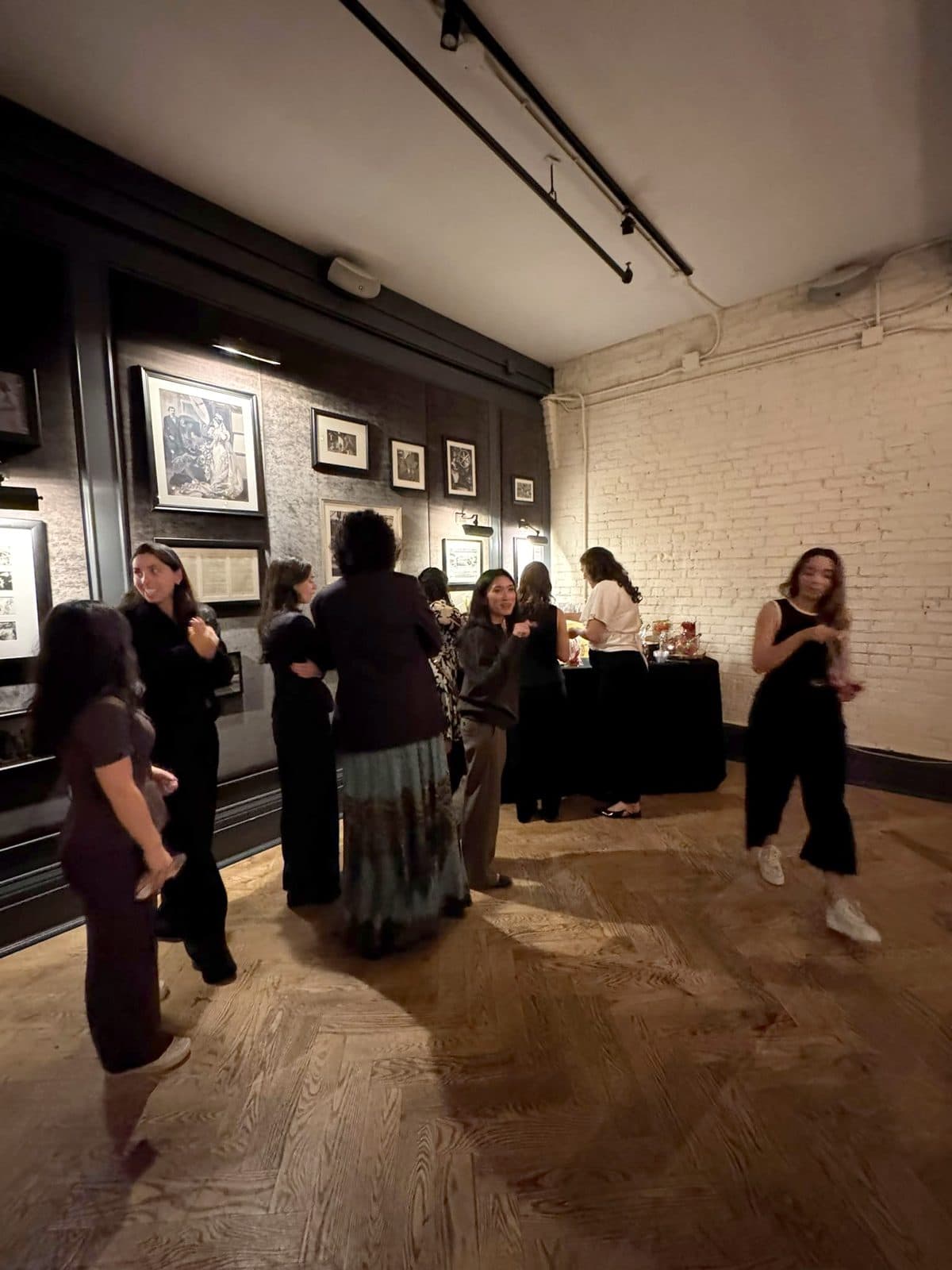 Guests standing in small groups on the herringbone floor beside the gallery wall.