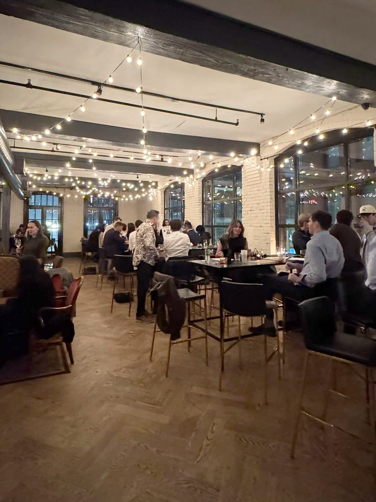 The second floor during the trivia night: guests at black high-top tables under string lights that run the length of the ceiling, the arched windows lit at the far end.