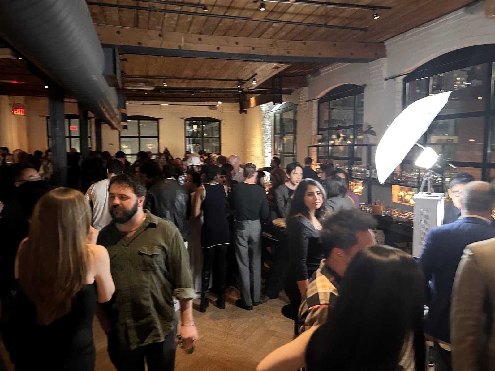 Guests crowded around the bar under the timber ceiling, with an umbrella light at the side of the room.