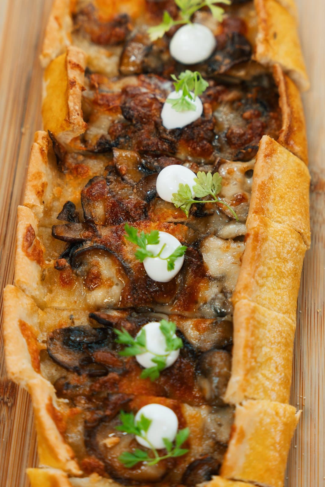 A long boat of pide bread filled with melted cheese and cremini mushrooms, topped with dots of crème fraiche and herb leaves.