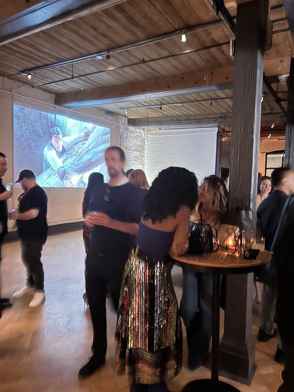 Guests at high tables while a film still is projected large onto the white brick wall behind them.