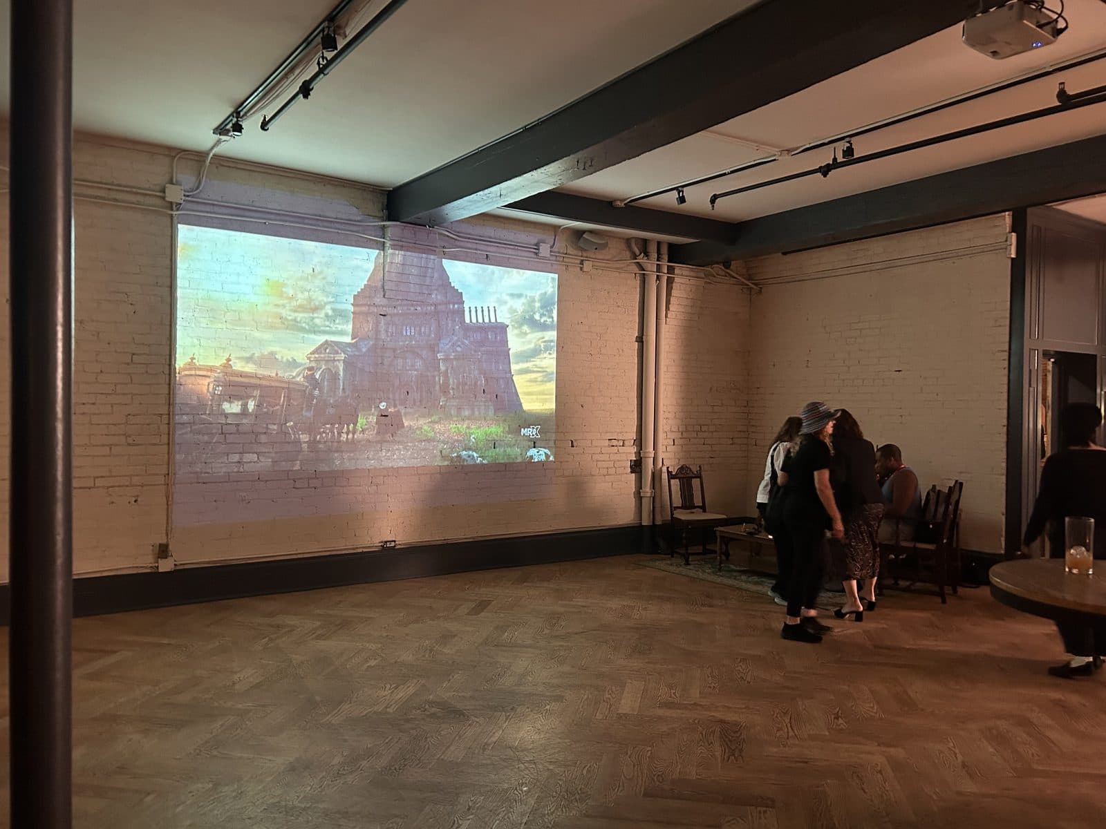 A quieter corner of the floor, the reel projected across the white brick wall above the herringbone floor.