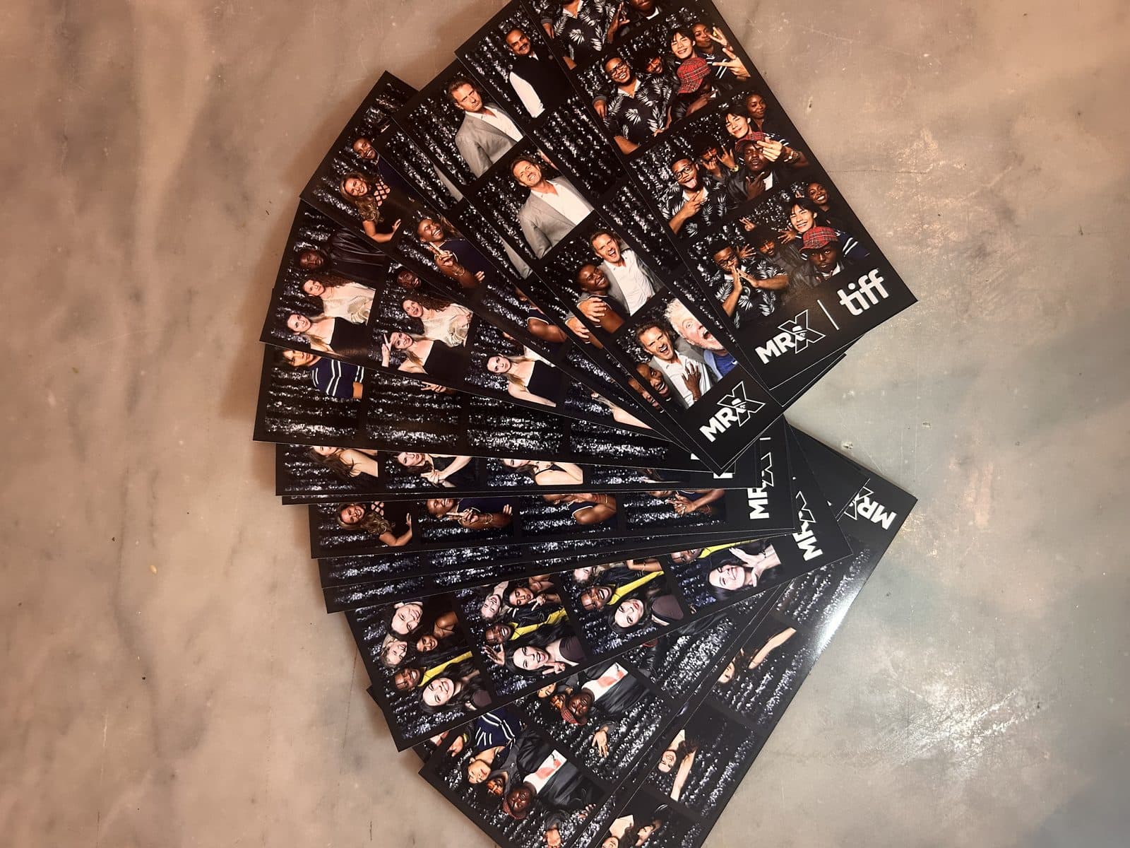 A fan of photobooth print strips on a marble surface, each strip branded with the MR. X and TIFF logos.