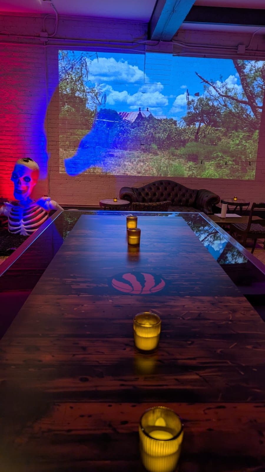 A long dark wooden table with candles down its length and the Raptors claw at its centre, a skeleton at the far end.