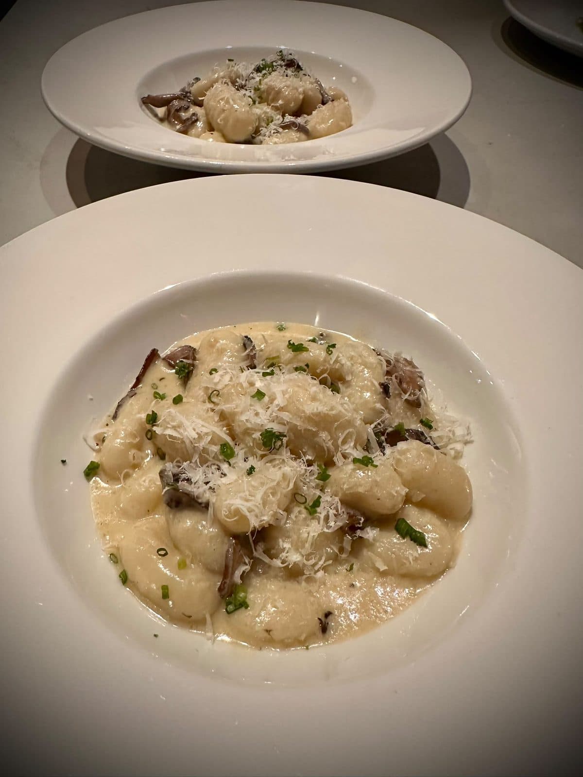Potato gnocchi in a creamy mushroom sauce in a wide white bowl, finished with chives and grated parmesan.