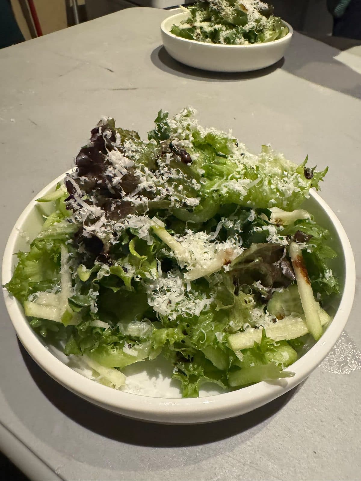 Mesclun salad in a white bowl, dressed leaves with thin slices of green apple and shaved parmesan on top.