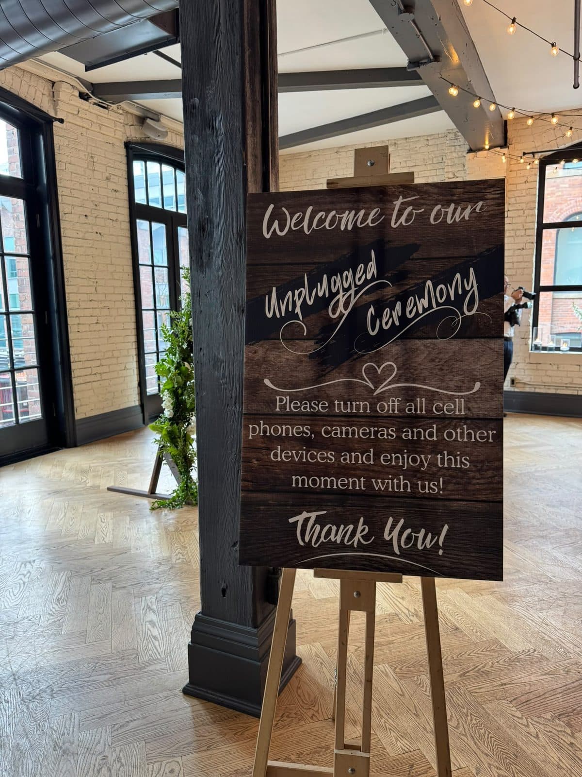 A wooden sign on an easel reading: Welcome to our unplugged ceremony. Please turn off all cell phones, cameras and other devices and enjoy this moment with us. Thank you.