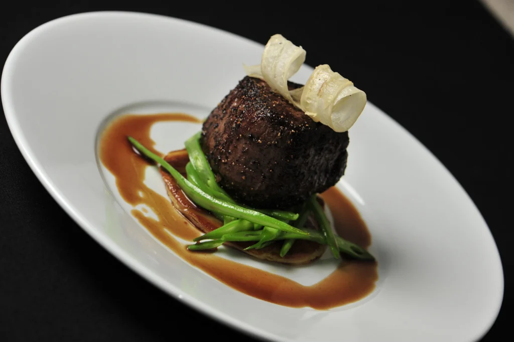 Plated fine dining dish at a corporate or wedding event, featuring steak with green beans and sauce on a white plate.