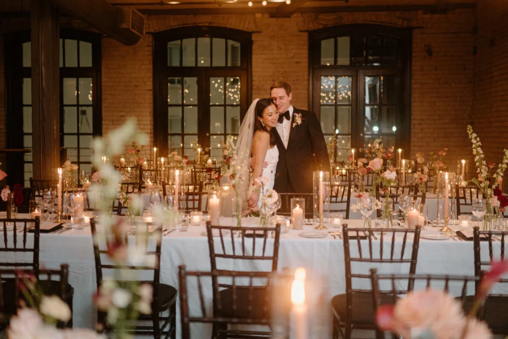 Indoor wedding reception with candlelit tables, romantic lighting, and newlywed couple posing