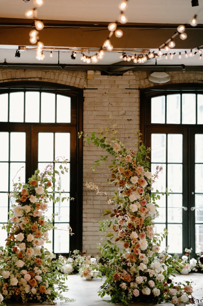 Indoor wedding setup with rose floral arrangements and hanging string lights.
