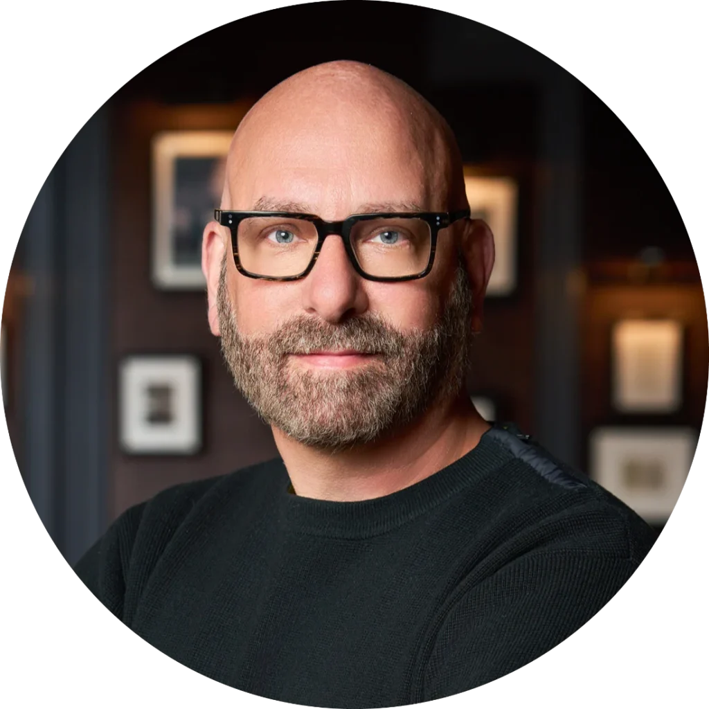 Professional headshot of a bald man with glasses and beard, part of the event leadership team.