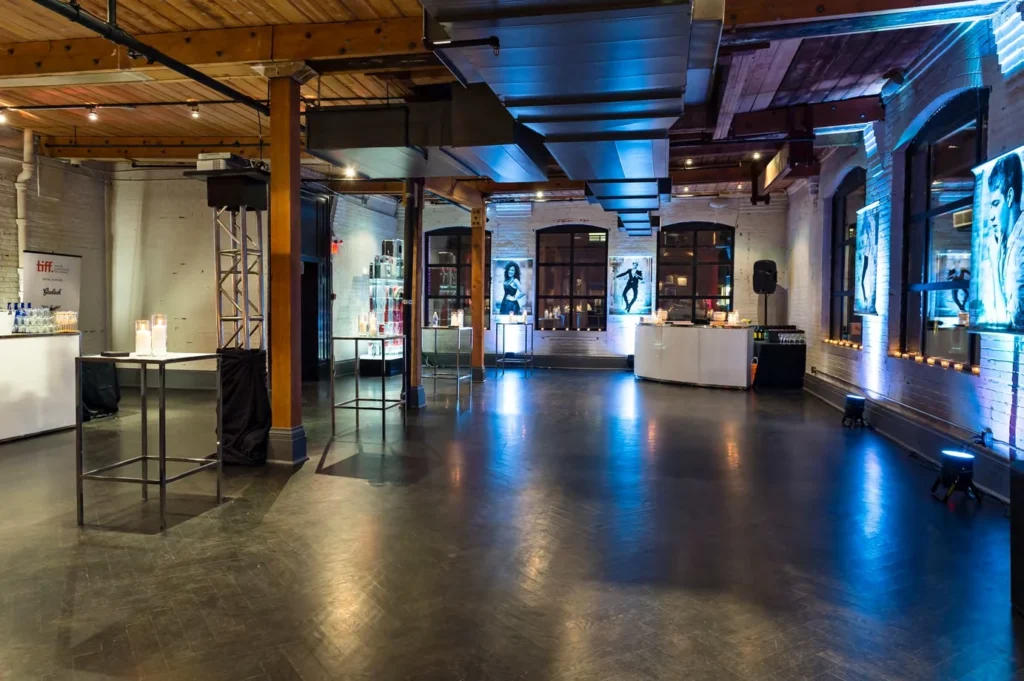 Spacious modern industrial event venue with exposed beams, high ceilings, and TIFF-themed cocktail setup—ideal for corporate events and photoshoots.