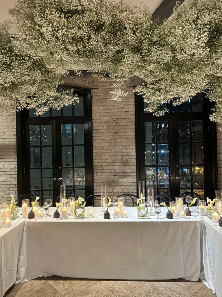Wedding reception table setting with candles, floral greenery, custom menus, and a linen tablecloth.