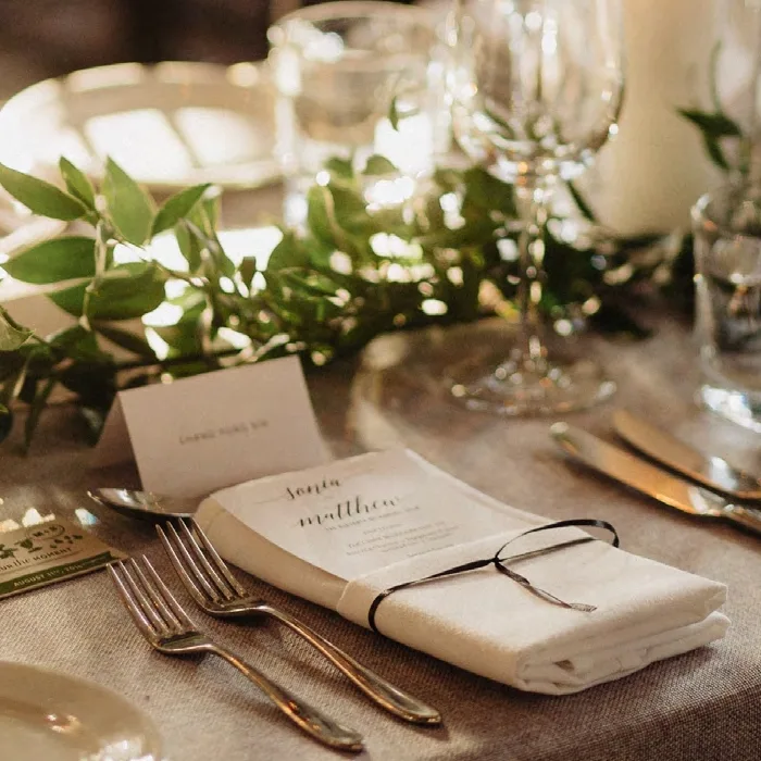 Wedding table setup featuring a guest name card, green foliage, and a tied menu on a plate